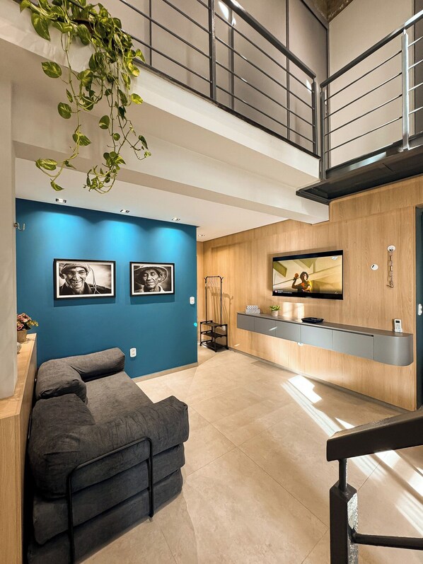 A modern living room with a sofa, a TV mounted on a wooden wall, and a staircase leading to an upper level.