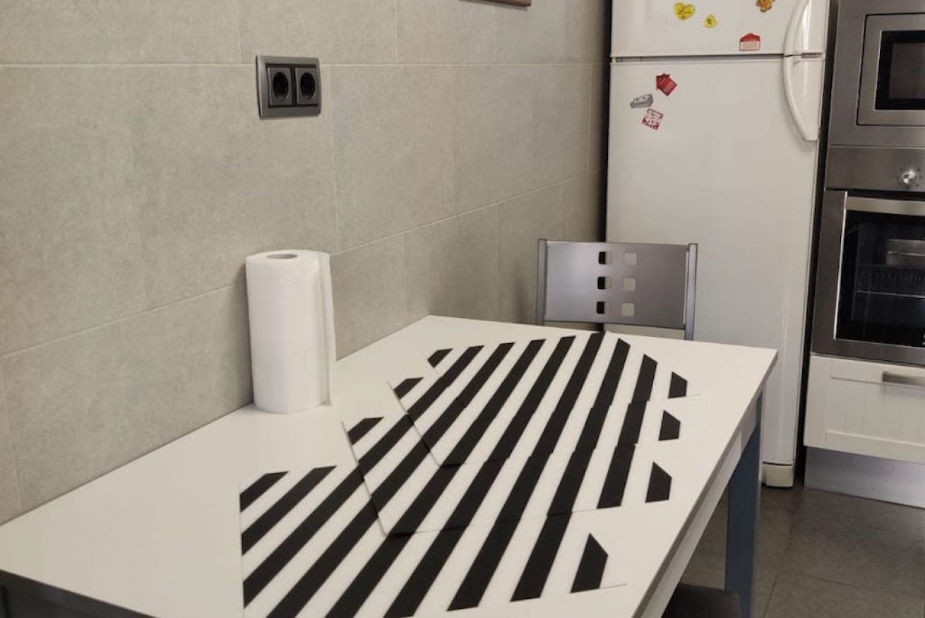 Eine Küche mit einem weißen Tisch, Küchenpapier, einem Stuhl und einem Kühlschrank mit Magneten.