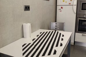 Eine Küche mit einem weißen Tisch, Küchenpapier, einem Stuhl und einem Kühlschrank mit Magneten.