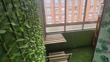 A room with a green leafy wall, a window with a view of a brick building, and a small wooden table.