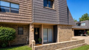 A two-story house with a brick facade, a front door with a welcome sign, and a small front yard with a bush. - Modern 3 Story Home 9 Min to DFW w King Suite Pool (Euless)