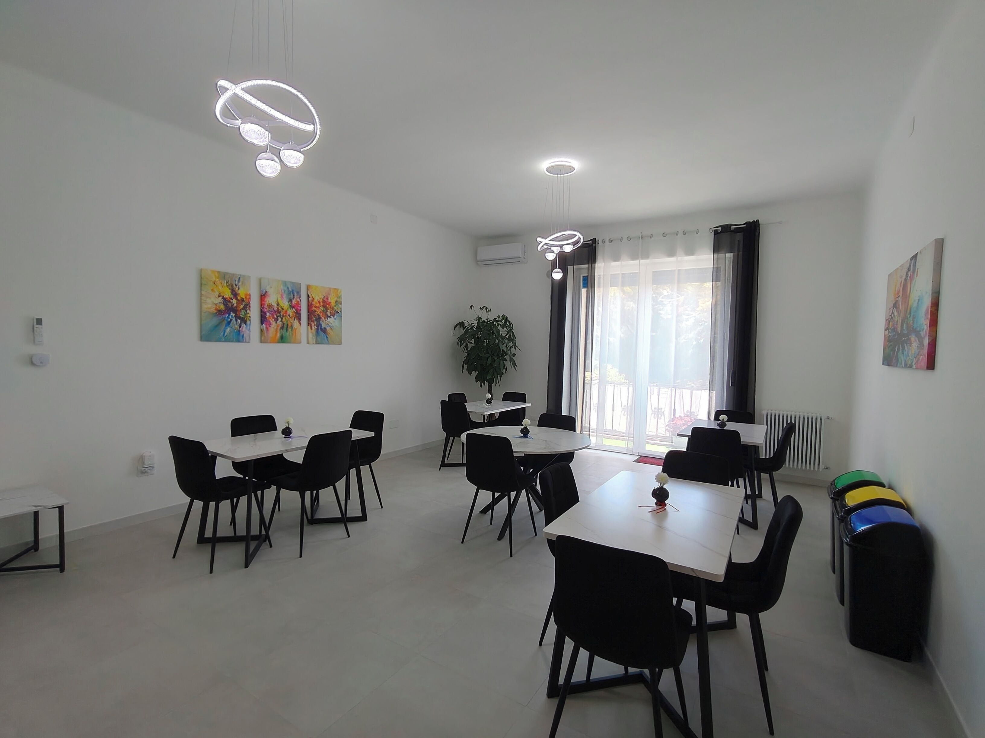 Un espace de restauration moderne, doté de plusieurs tables et chaises, d’un éclairage au plafond et de peintures abstraites accrochées aux murs.
