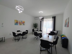 Et moderne spiseområde med flere borde og stole, loftslamper og abstrakte malerier på væggene.