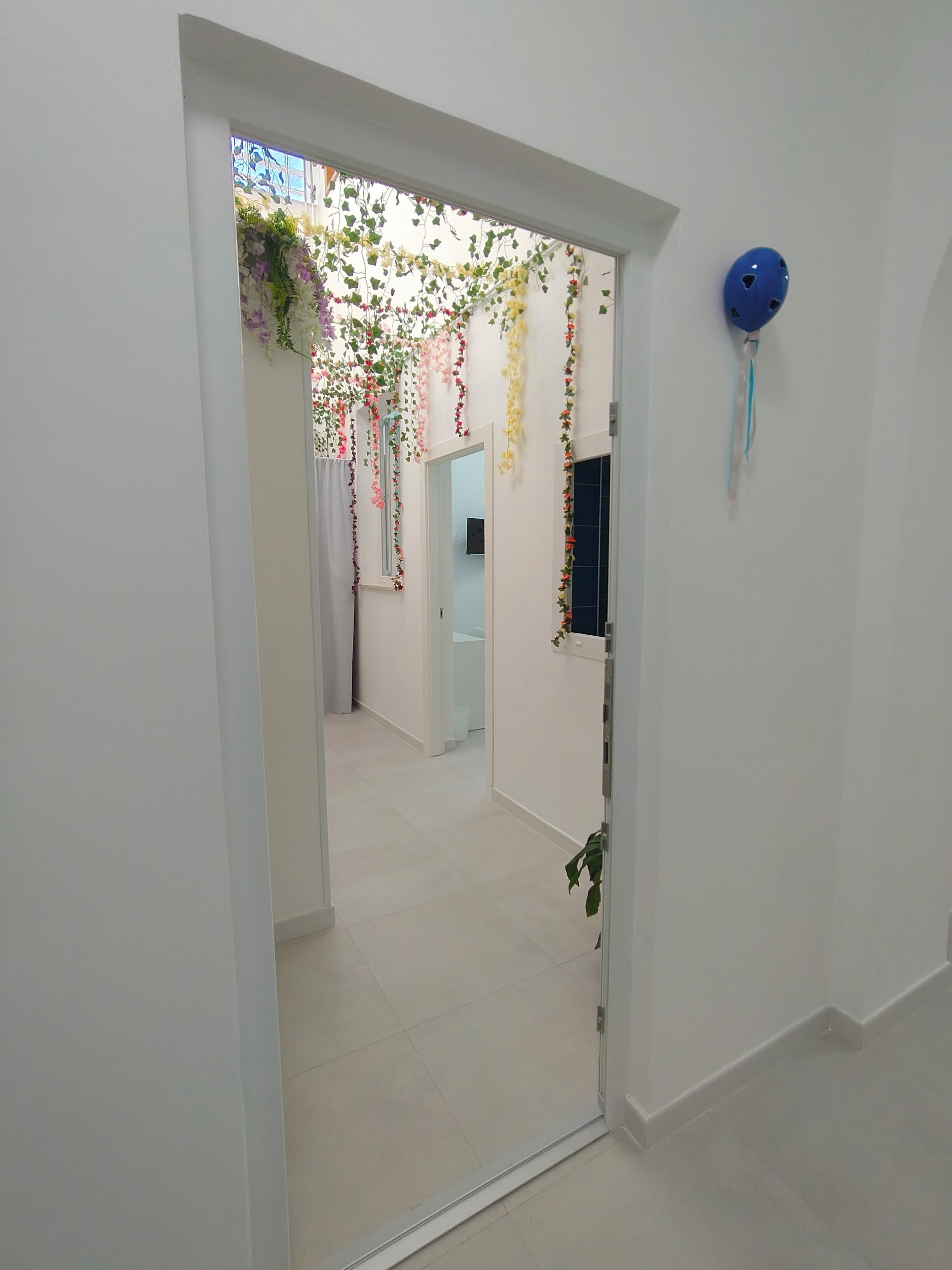Un couloir avec une porte blanche, un objet bleu accroché au mur et des décorations florales suspendues.