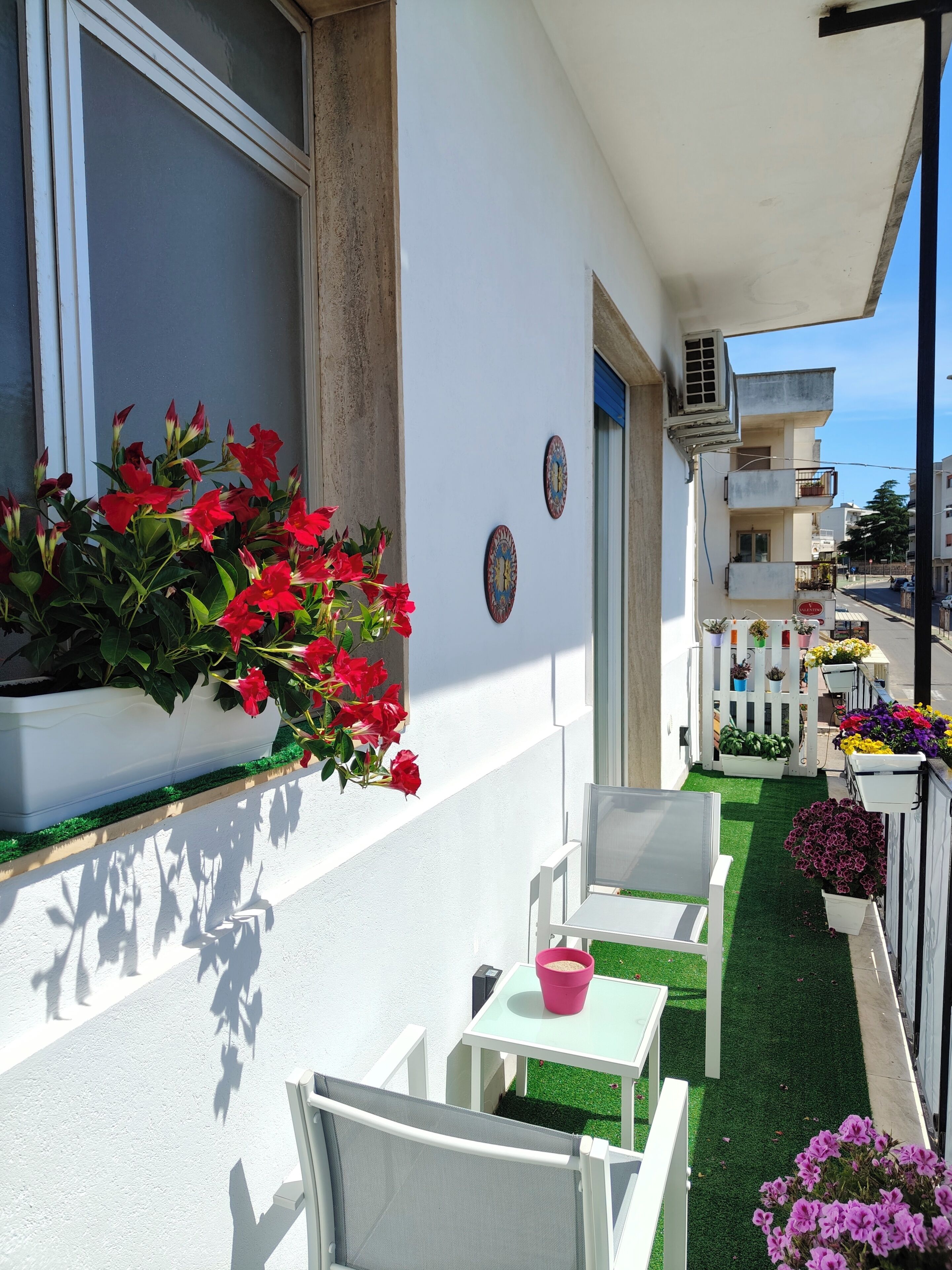 Un balcon avec des chaises blanches, une petite table et des plantes en pot.