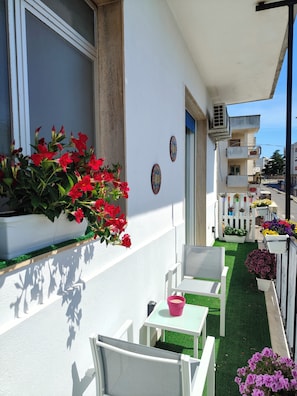 Un balcon avec des chaises blanches, une petite table et des plantes en pot.