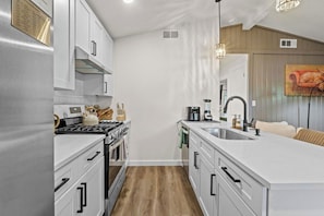 A modern kitchen with white cabinetry, a central island, and a built-in oven. - Cozy Austin Getaway | Game Room + Large Backyard (Austin)
