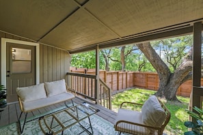 A covered patio with a wicker sofa, a metal table, and a wooden chair. - Cozy Austin Getaway | Game Room + Large Backyard (Austin)