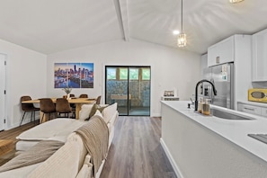 A modern kitchen with a built-in island, a dining area with a table and chairs, and a cityscape painting on the wall. - Cozy Austin Getaway | Game Room + Large Backyard (Austin)
