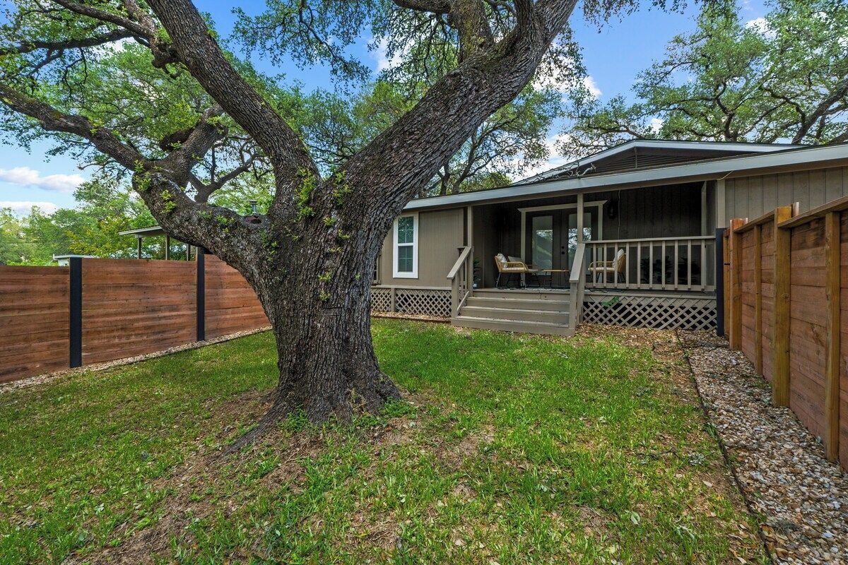 A single-story house with a porch, a large tree in front, and a wooden fence.