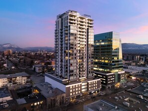 A high-rise building with multiple balconies, a glass facade, and a view of a cityscape with mountains in the background.