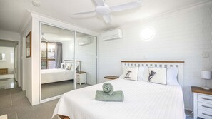 Ein Hotelzimmer mit einem großen Bett, einem Deckenventilator, einem Spiegel und einer Schiebetür, die auf einen Balkon führt.