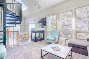 Ein modernes Wohnzimmer mit Kamin, Fernseher, einer Treppe und großen Fenstern.