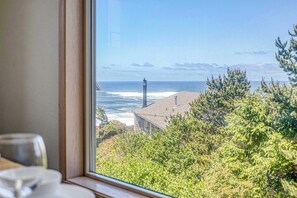 Blick durch ein Fenster auf ein Küsteneigentum mit Leuchtturm, Ozean und dichtem Grün.