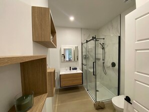 A modern bathroom with a glass shower enclosure, a wooden vanity, and a white toilet. - Le Relais Austin 4 — Spa, Nature & Adventure (Austin)