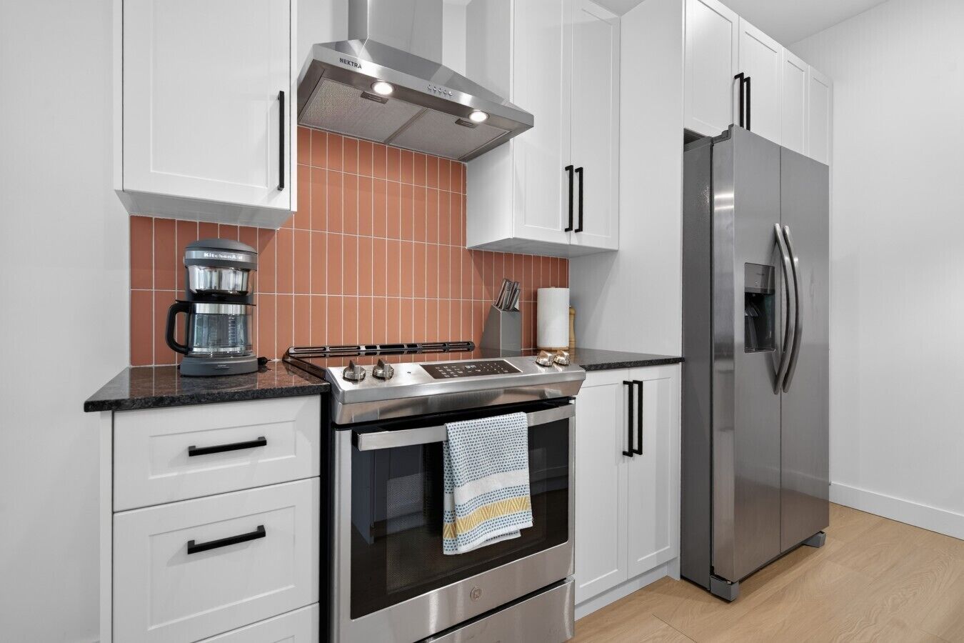 Une cuisine moderne avec des meubles blancs, une cuisinière en acier inoxydable, une machine à café et un réfrigérateur.