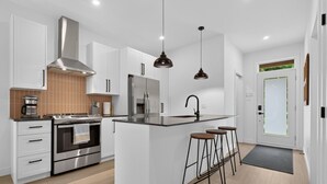 A modern kitchen with white cabinets, stainless steel appliances, and a central island with stools. - Le Relais Austin 4 — Spa, Nature & Adventure (Austin)