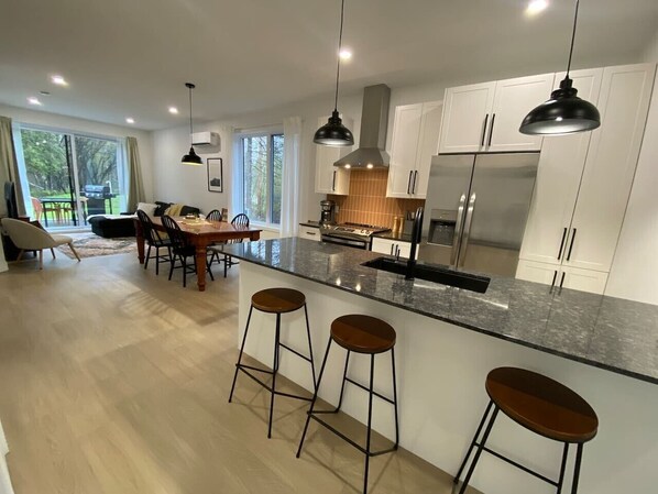 A modern kitchen with a large island, bar stools, and a dining area with a table and chairs. - Le Relais Austin 4 — Spa, Nature & Adventure (Austin)