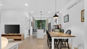Een moderne woonkamer met een televisie, een houten tv-meubel en een eethoek met een houten tafel en stoelen.