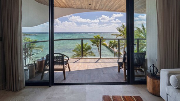 Ein Balkon mit Blick auf den Ozean, ausgestattet mit Stühlen und einem Tisch, sowie eine Schiebeglastür.