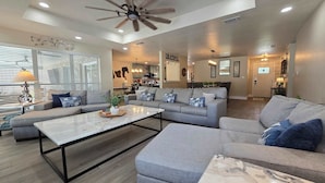 A spacious living room with a large gray sectional sofa, a white coffee table, and a ceiling fan. - Gruene Gables Pool & Game Room (New Braunfels)