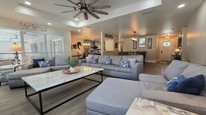 A spacious living room with a large gray sectional sofa, a white coffee table, and a ceiling fan. - Gruene Gables Pool & Game Room (New Braunfels)