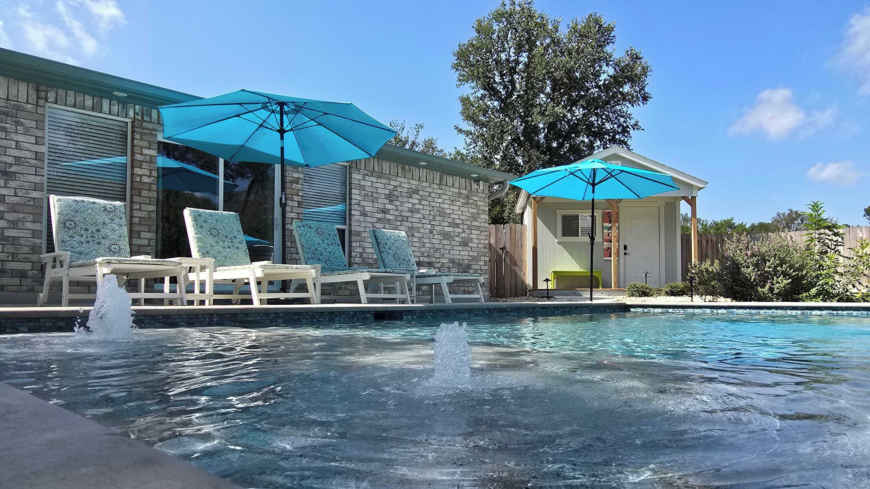 Une piscine avec des chaises longues et des parasols, un mur en briques et un espace abrité.