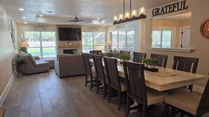 A dining area with a long table, chairs, and a ceiling fan. - Gruene Gables Pool & Game Room (New Braunfels)