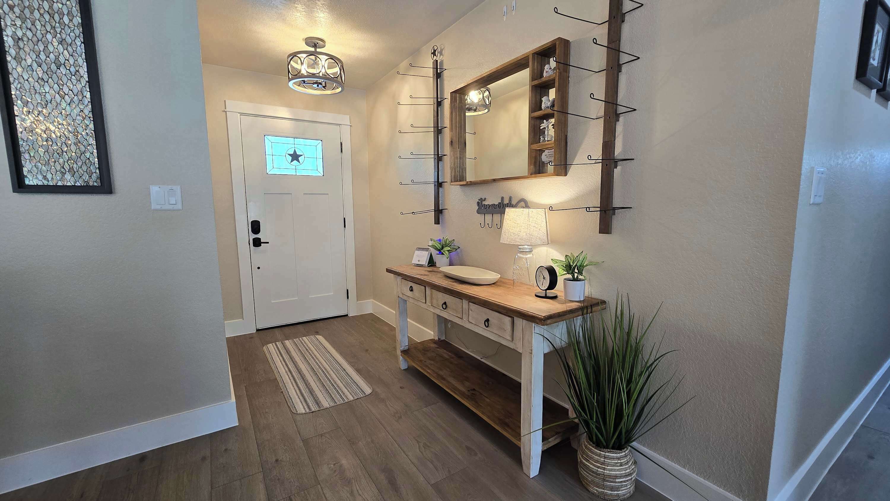 A hallway with a wooden bench, a wall-mounted mirror, a door with a star-shaped light, and a potted plant.