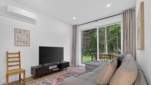 A living room with a sofa, TV, wooden chair, and a large window with curtains.