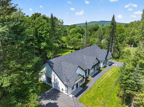 A two-story house with a sloped roof, surrounded by dense greenery and trees.