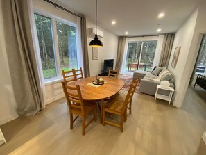A dining area with a round wooden table and chairs, a pendant light, and a sofa in the background. - Le Relais Austin 1 — Spa, Nature & Adventure (Austin)
