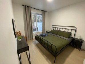 Un dormitorio con una cama, una mesita de noche, una silla, una pequeña mesa con una planta y una ventana con cortinas.