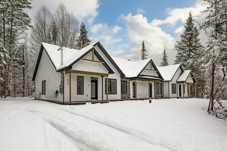 A row of three cabins with gabled roofs, set in a snowy forest.. Le Relais Austin 1 — Spa, Nature & Adventure