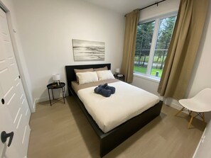 A bedroom with a bed, a nightstand, a chair, a window with curtains, and a painting on the wall. - Le Relais Austin 1 — Spa, Nature & Adventure (Austin)