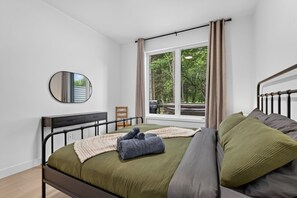 A bedroom with a bed, a bedside table, a mirror, and a window with curtains.