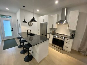 Una cocina moderna con una isla central, electrodomésticos de acero inoxidable e iluminación colgante.