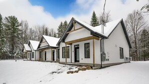 En rad vita stugor med sadeltak, placerade i ett snöigt landskap med träd i bakgrunden.
