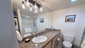 A bathroom with a granite countertop, a white sink, a toilet, a trash can, and a shower. - Cozy 1-bedroom condo in serene Reno with fitness room and AC (Reno)