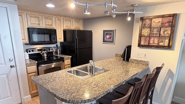 A kitchen with granite countertops, stainless steel appliances, wooden cabinets, a built-in microwave, and a bar area with stools. - Cozy 1-bedroom condo in serene Reno with fitness room and AC (Reno)