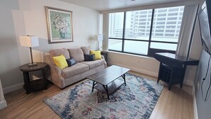 A living room with a sofa, two lamps, a coffee table, a rug, and a large window. - Cozy 1-bedroom condo in serene Reno with fitness room and AC (Reno)