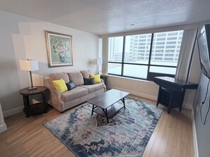 Ein Wohnzimmer mit einer Couch, zwei Lampen, einem Couchtisch, einem Teppich und einem großen Fenster.