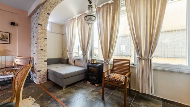 Ein Wohnzimmer mit Sofa, Sessel, Kamin und einem großen Fenster mit Vorhängen.