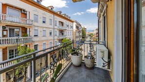 Ein Balkon mit Metallgeländer, Blumentöpfen und Blick auf benachbarte Gebäude.