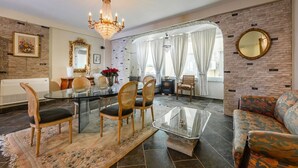 Ein Wohnzimmer mit einem Glastisch, Holzsesseln, einer Couch, einer Pendelleuchte und einem Kamin.