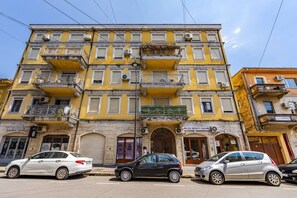 Ein mehrstöckiges Gebäude mit einer gelben Fassade, ein Geschäft im Erdgeschoss und geparkte Autos davor.