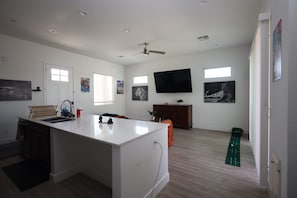 Eine moderne Küche mit Kochinsel, Essbereich mit Sofa, Wand-Fernseher und Fenster für natürliches Licht.