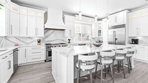 A modern kitchen with white cabinetry, a central island with bar stools, stainless steel appliances, and a marble backsplash. - Miramar Beach Home, Pool, Hot Tub & Chef's Kitchen (Miramar Beach)