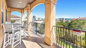 A balcony with a table and chairs, a metal railing, and a view of the ocean and buildings. - Miramar Beach Home, Pool, Hot Tub & Chef's Kitchen (Miramar Beach)