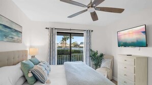 Un dormitorio con cama, cómoda, televisor, ventilador de techo y ventana con cortinas.